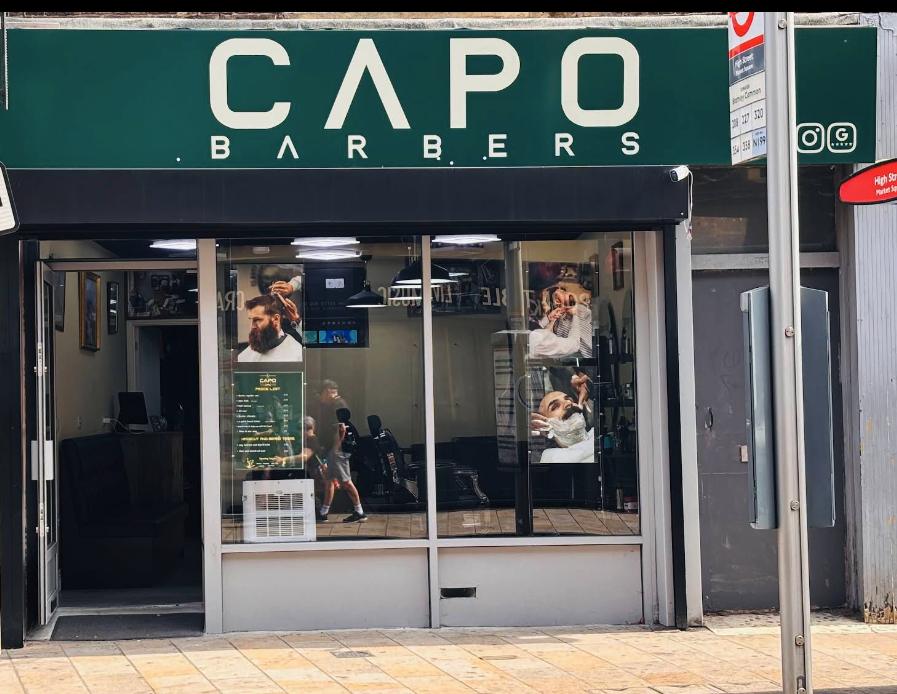 Shopfront of Capo barbers on High Street, with a green sign and cream lettering